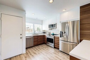 A modern kitchen with white cabinets, stainless steel appliances, and a wooden floor. - Contemporary Condo | Mountain Views & Balcony | 1 Block to Beach (Carpinteria)