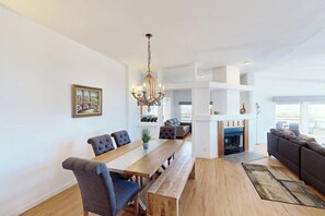Amplia sala de estar con una mesa de comedor de madera, sillas tapizadas de color gris, un sofá gris, chimenea y un candelabro.