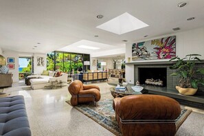 Ein modernes Wohnzimmer mit Kamin, Ledersofas und einem großen Fenster mit Blick auf Grünflächen.