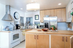 A modern kitchen with a central island, stainless steel appliances, wooden cabinets, and a hanging light fixture.