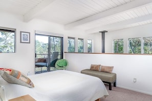 A bedroom with a bed, a bench, and large windows.