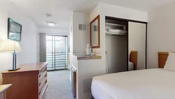 A hotel room with a bed, a desk with drawers, a mirror, a wardrobe, and a window with blinds.