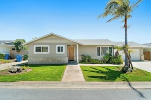 A single-story house with a front porch, a small front yard with a palm tree, and a garage.
