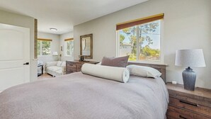 Een slaapkamer met een groot bed, een bureau, een stoel, een lamp en een raam met uitzicht op bomen.