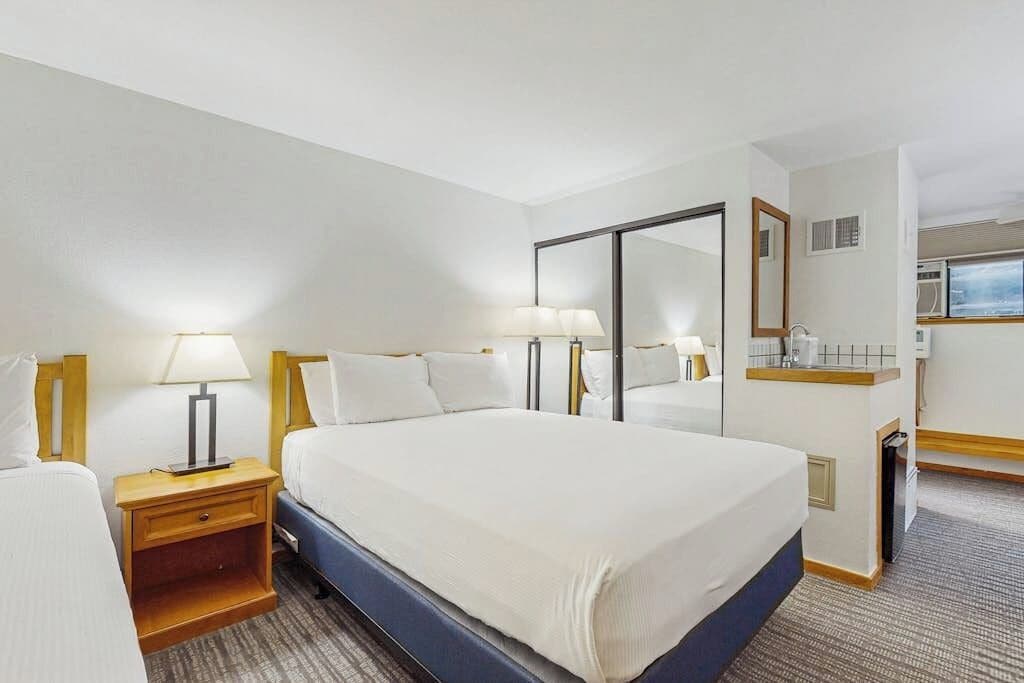 Habitación de hotel con una cama grande, dos mesitas de noche con lámparas, un espejo, un escritorio pequeño con una silla y una ventana.