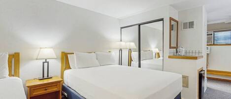 Habitación de hotel con una cama grande, dos mesitas de noche con lámparas, un espejo, un escritorio pequeño con una silla y una ventana.