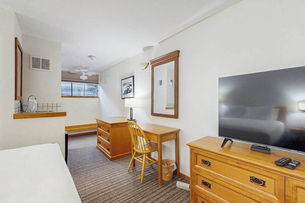 A hotel room with a bed, a desk with a chair, a television, a dresser, and a window.