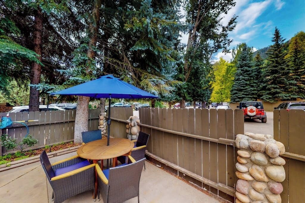 An outdoor patio with a round table and chairs, a blue umbrella, and a stone wall.