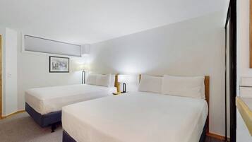 A hotel room with two beds, a framed picture on the wall, and a lamp on the nightstand.