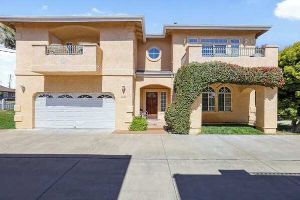A two-story house with a garage, a balcony, and an archway covered with climbing plants.