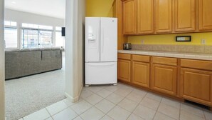 A kitchen with wooden cabinets, a white refrigerator, and a gray sofa in the adjacent living area. - Dog-friendly home near beach with fireplace, grill, yard, & W/D (Grover Beach)