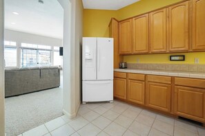 Una cocina con armarios de madera, un refrigerador blanco y un sofá gris en la zona de estar contigua.