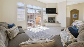 A living room with a fireplace, a television mounted above it, and a sliding glass door leading to a patio. - Dog-friendly home near beach with fireplace, grill, yard, & W/D (Grover Beach)