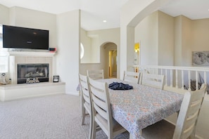 A dining area with a table set for four, a fireplace, and a television mounted above it.