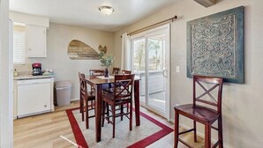 A dining area with a table and chairs, a kitchen with a dishwasher, and a sliding glass door leading to a balcony. - Terrific home close to the beach, restaurants, parks, and activities w/free WiFi (Grover Beach)