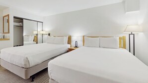 Une chambre d’hôtel avec deux lits, un miroir, des lampes de chevet et une armoire.