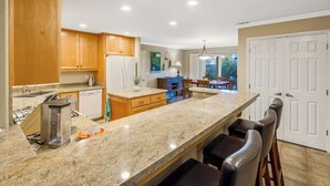 A kitchen with granite countertops, wooden cabinets, a built-in oven, and a bar area with stools. - Comfortable home near beach with enclosed yard & patio, W/D, grill (Arroyo Grande)
