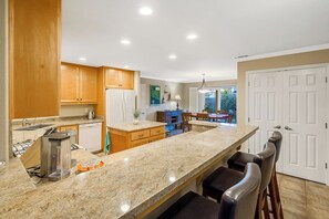 Eine Küche mit Granit Arbeitsplatten, Holzschränken, einem eingebauten Backofen und einer Bar mit Hockern.