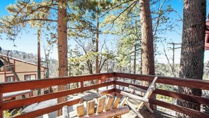 A wooden deck with a bench, surrounded by tall trees and a building in the background.