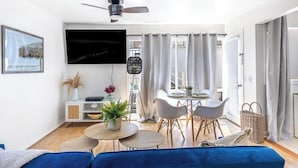 Ein modernes Wohnzimmer mit Flachbildfernseher, Deckenventilator, Essbereich mit Tisch und Stühlen sowie einer Couch.