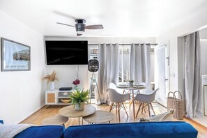 Ein modernes Wohnzimmer mit Flachbildfernseher, Deckenventilator, Essbereich mit Tisch und Stühlen sowie einer Couch.