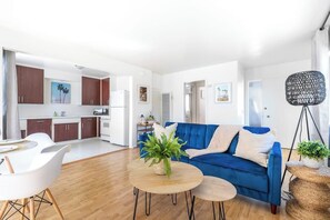 A modern living room with a blue sofa, a coffee table, and a dining area with white chairs.