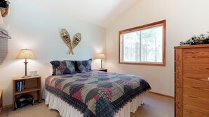 Une chambre à coucher avec un grand lit, deux lampes de chevet, une commode en bois et une fenêtre donnant sur des arbres.