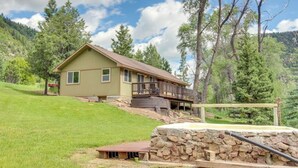 Une maison avec des fondations en pierre, une terrasse en bois et une colline verdoyante.