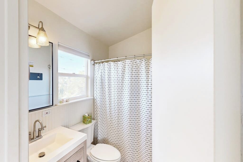 Une salle de bain avec un lavabo blanc, des toilettes, une fenêtre et un rideau de douche.