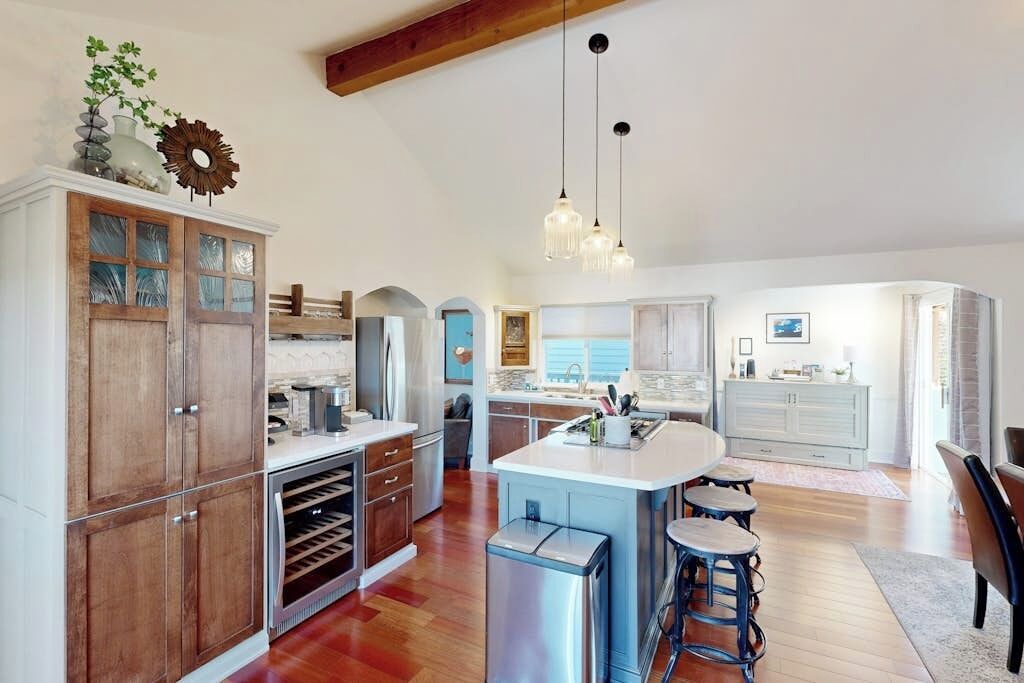 A spacious kitchen with wooden cabinets, a central island, bar stools, and pendant lighting.