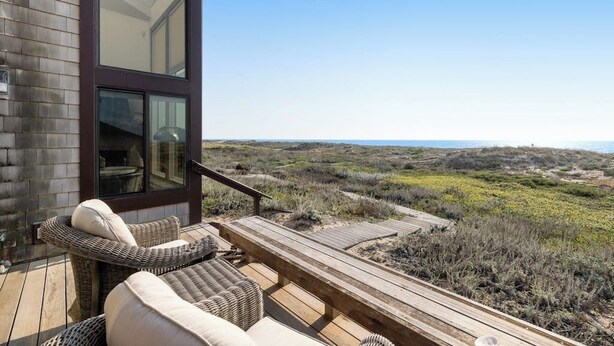 Een modern gebouw met een terras, rieten meubilair en uitzicht op het strand.