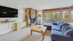Un salon avec un mur en pierre, un téléviseur à écran plat, un canapé, une table basse et un balcon avec vue.