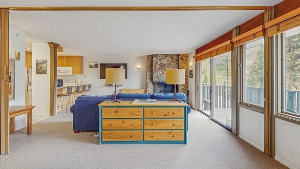 Une chambre moderne avec un grand lit, une commode en bois, un bureau et une vue sur l’extérieur grâce à de grandes fenêtres.