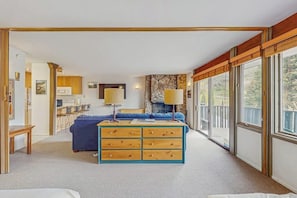 A modern bedroom with a large bed, a wooden dresser, a desk, and a view of the outdoors through large windows.