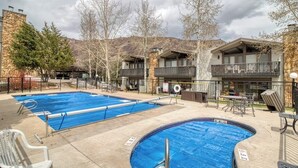 Un espace piscine comprenant deux piscines, des sièges extérieurs et un bâtiment doté de balcons.