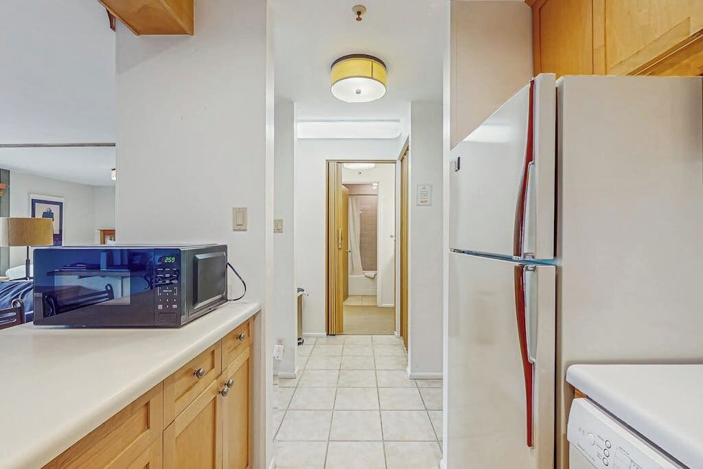 A kitchen with a microwave, refrigerator, wooden cabinets, and a tiled floor.