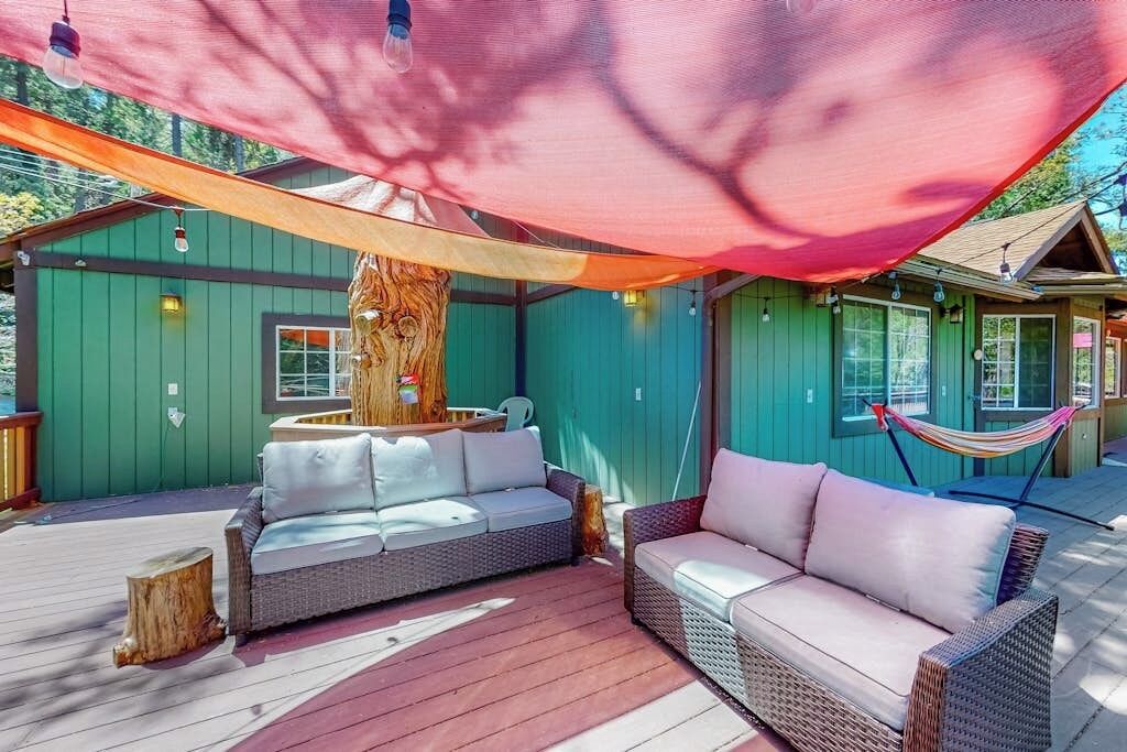 A covered outdoor seating area with wicker furniture, a hammock, and a wooden tree stump.