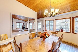 Ein Esszimmer mit Holztisch, Stühlen, einer Chandelier und großen Fenstern.
