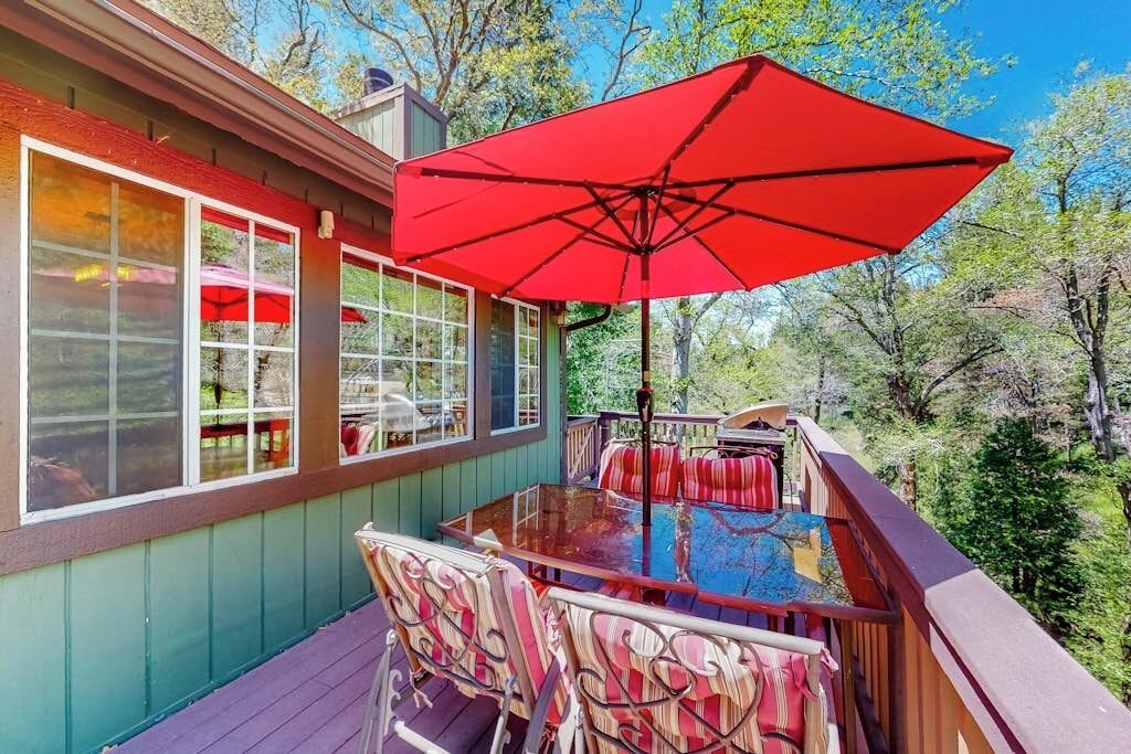 Une terrasse dotée d’une table à plateau en verre, d’un parasol rouge et de chaises en osier.