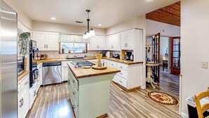 Una cocina moderna con armarios blancos, una isla de madera, electrodomésticos de acero inoxidable y techo de madera.