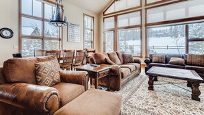 A spacious living room with leather sofas, a coffee table, and large windows offering a view of a snowy landscape.