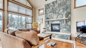 A cozy living room with a stone fireplace, large windows, and a comfortable seating area.
