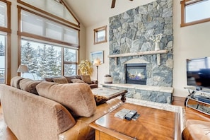 A cozy living room with a stone fireplace, large windows, and a comfortable seating area. - Mountain retreat overlooking Breck Golf Course with hot tub, free WiFi, & W/D (Breckenridge)