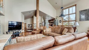 A spacious living room with a large leather sofa, a flat-screen TV, and a dining area with a table and chairs.