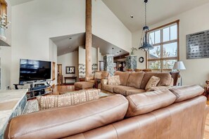A spacious living room with a large leather sofa, a flat-screen TV, and a dining area with a table and chairs. - Mountain retreat overlooking Breck Golf Course with hot tub, free WiFi, & W/D (Breckenridge)