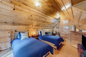 Ein schlicht eingerichtetes Schlafzimmer im Blockhausstil mit zwei Betten, Holzwänden, einer Deckenleuchte, einem Schreibtisch und einem Stuhl.