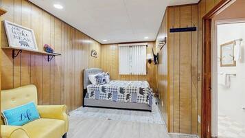 A bedroom with a bed, a yellow armchair, wooden paneling, a clock, and a door.