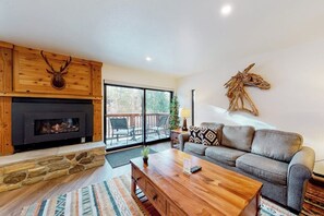 A living room with a fireplace, a sofa, a coffee table, and a large window. - Inviting ski-in condo with fireplace, hot tubs, & gym (Breckenridge)
