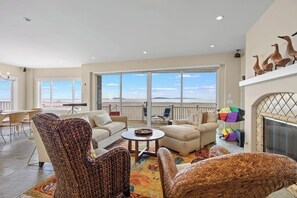 Ein geräumiges Wohnzimmer mit großem Fenster und Ausblick auf eine reizvolle Landschaft, inklusive Kamin und Korbmöbeln.
