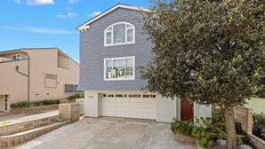 A two-story residential building with a garage, a tree in the front yard, and a clear sky. - Beachfront abode with spacious deck, pool table, gas grill, smart TVs, & W/D (Oxnard)